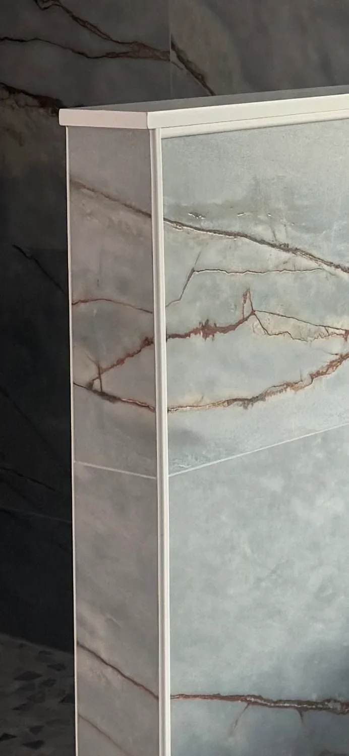 Large-format marble tile with natural veining, white trim frame, and professional grout lines