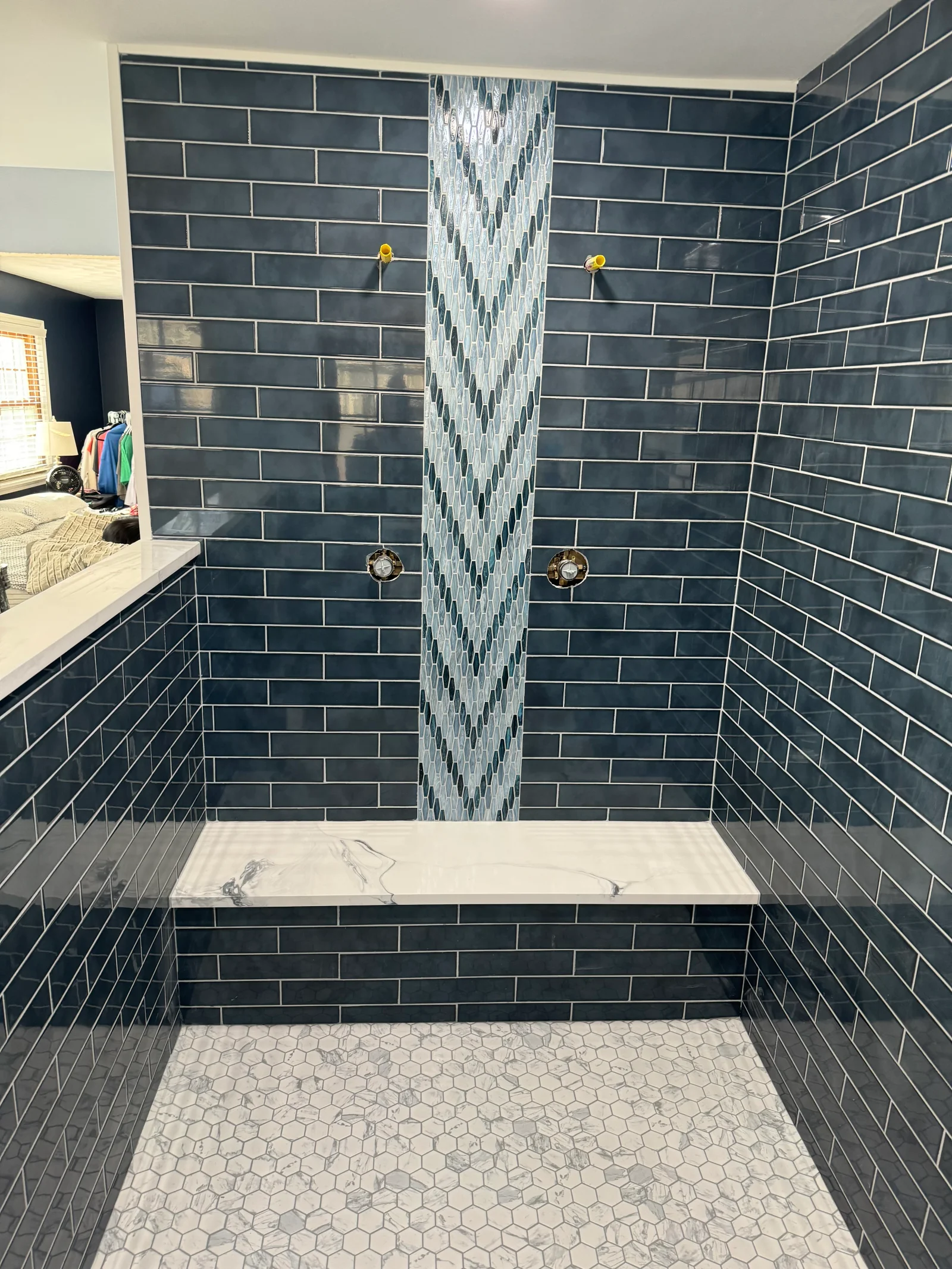 Dark blue subway tile shower with glass mosaic accent strip, marble bench, and hexagonal floor tile