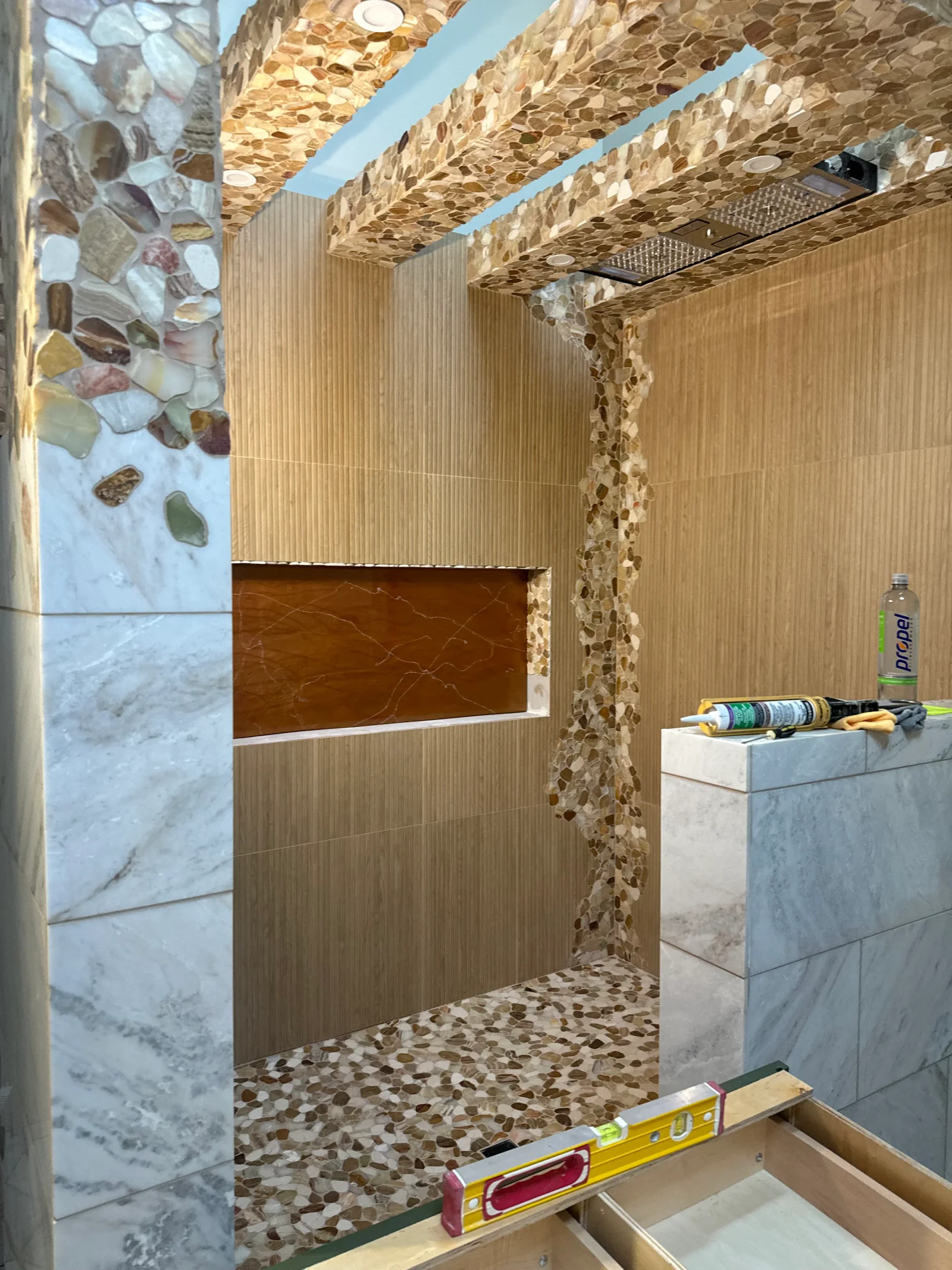 Walk-in shower with marble tile walls, river rock mosaic floor and ceiling, brown accent band