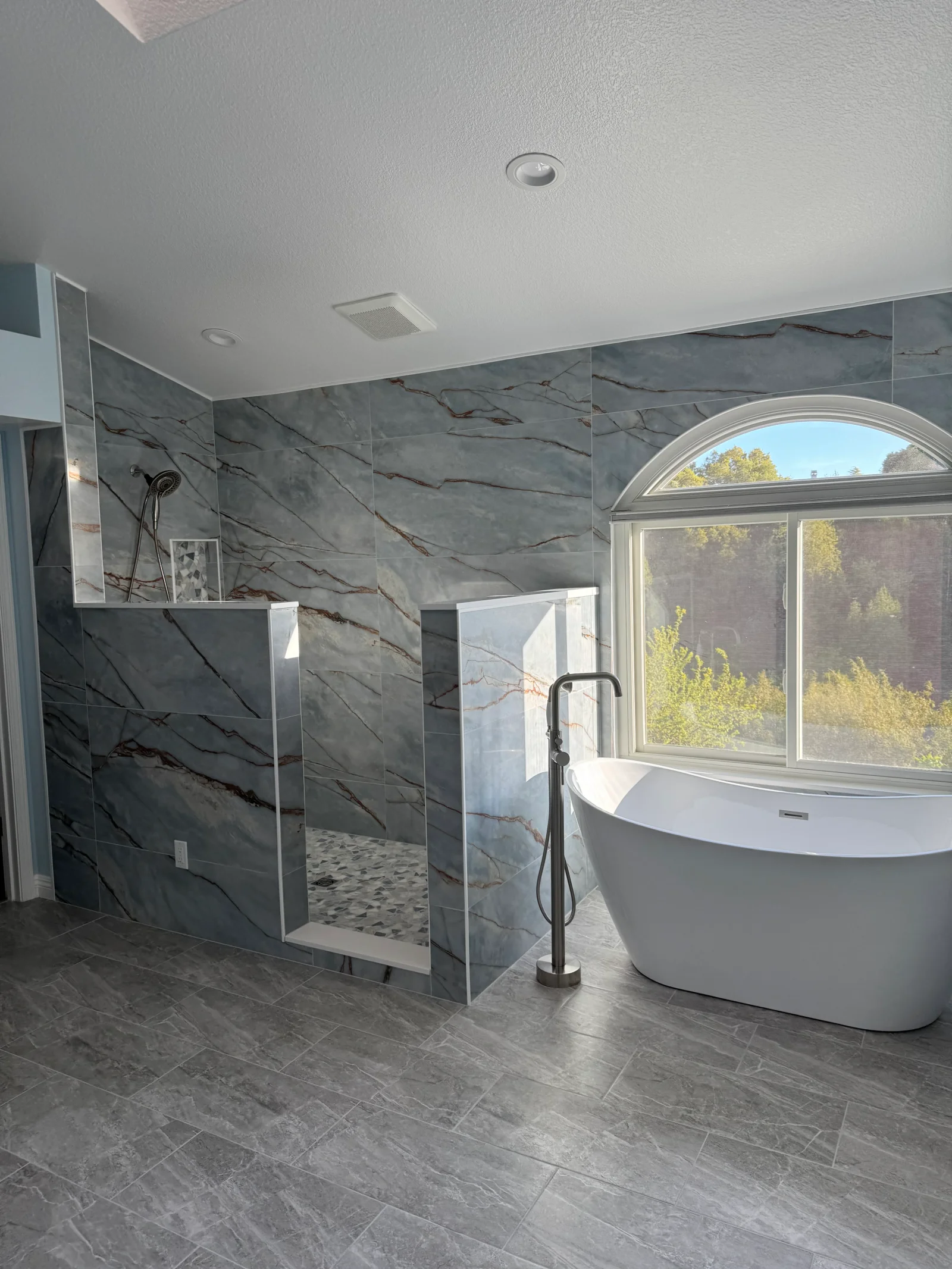 Modern bathroom with marble tile shower enclosure, freestanding tub, and gray tile flooring