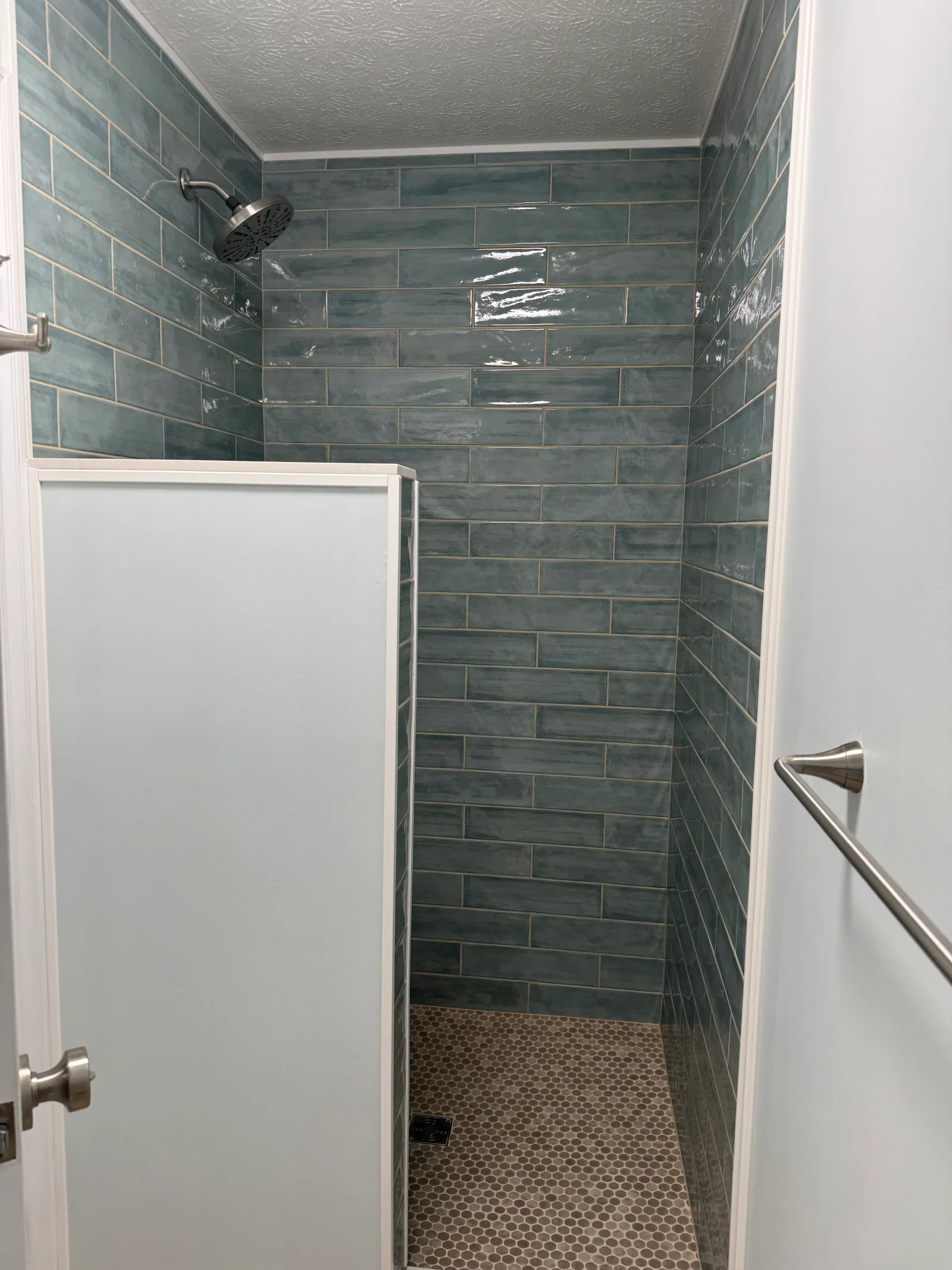Teal subway tile shower with hexagonal floor tile, frameless glass door, and brushed nickel fixtures