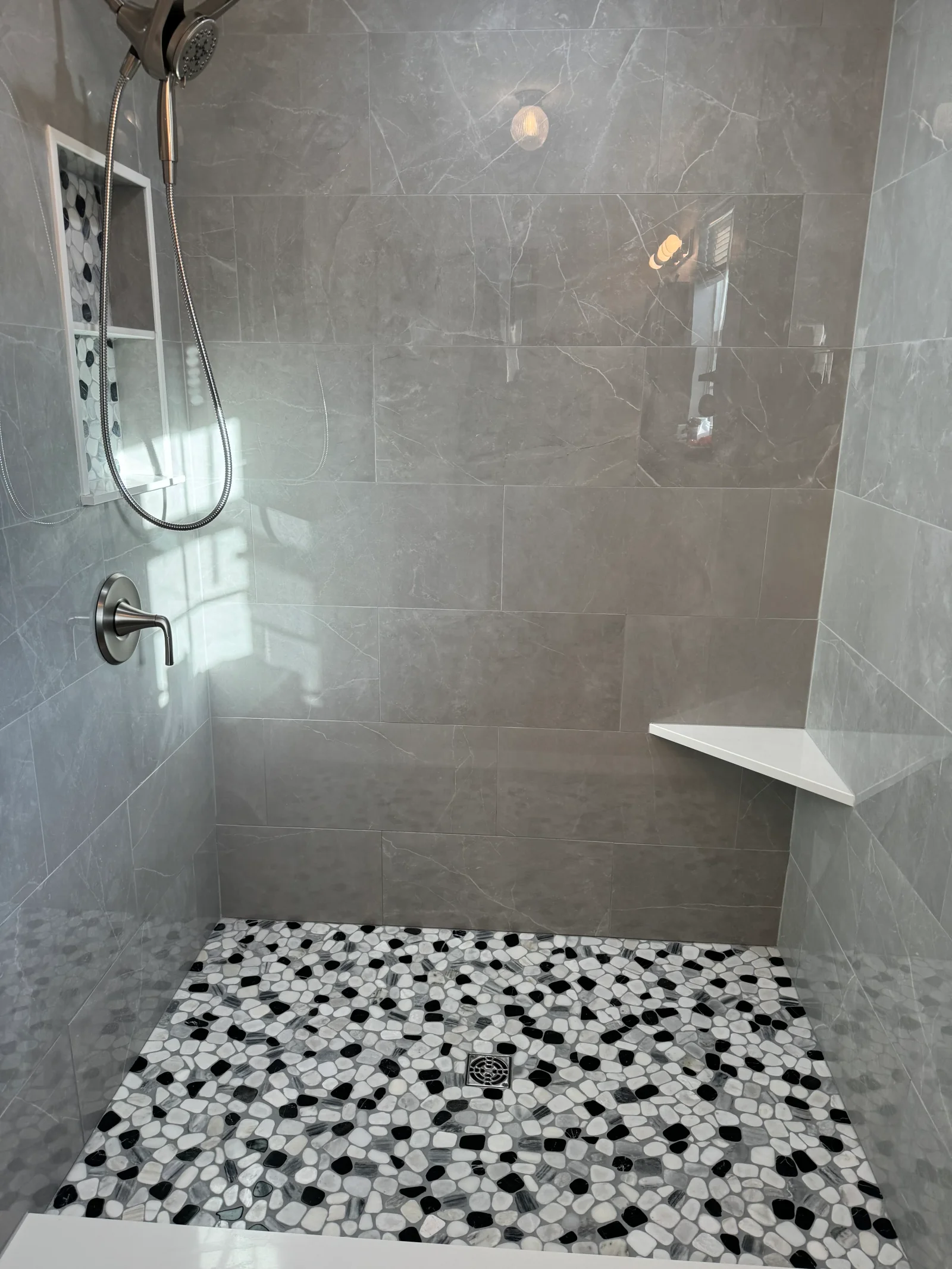 Gray marble tile shower with black and white hexagonal mosaic floor and frameless glass door