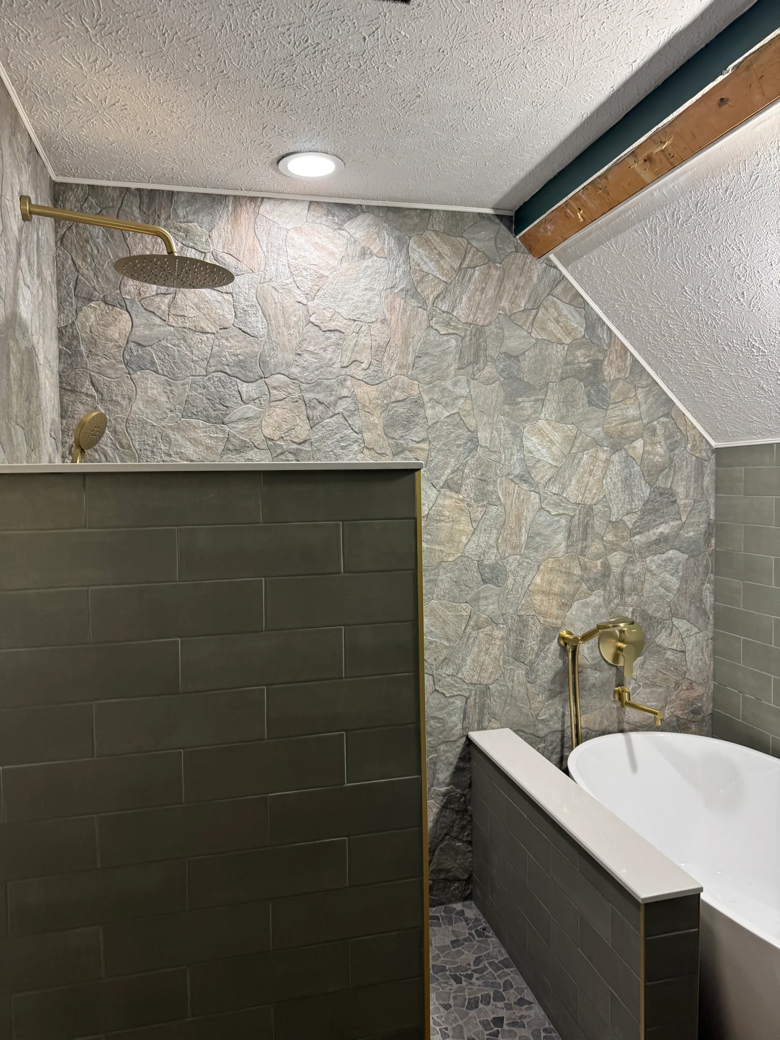 Walk-in shower with slate tile surround, dark green subway tile, brass showerhead and fixtures, stone accent wall