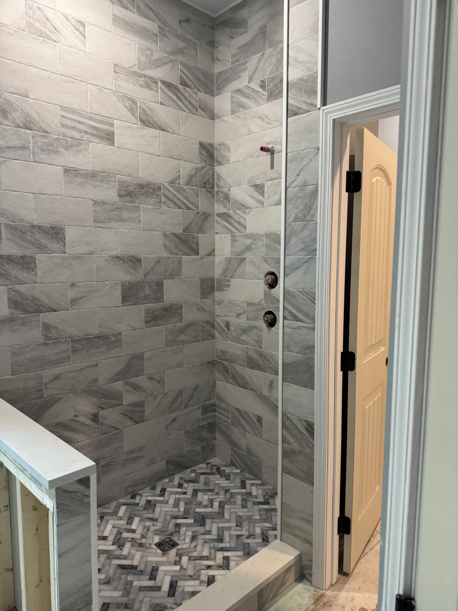 Marble subway tile shower with herringbone floor pattern and frameless glass door