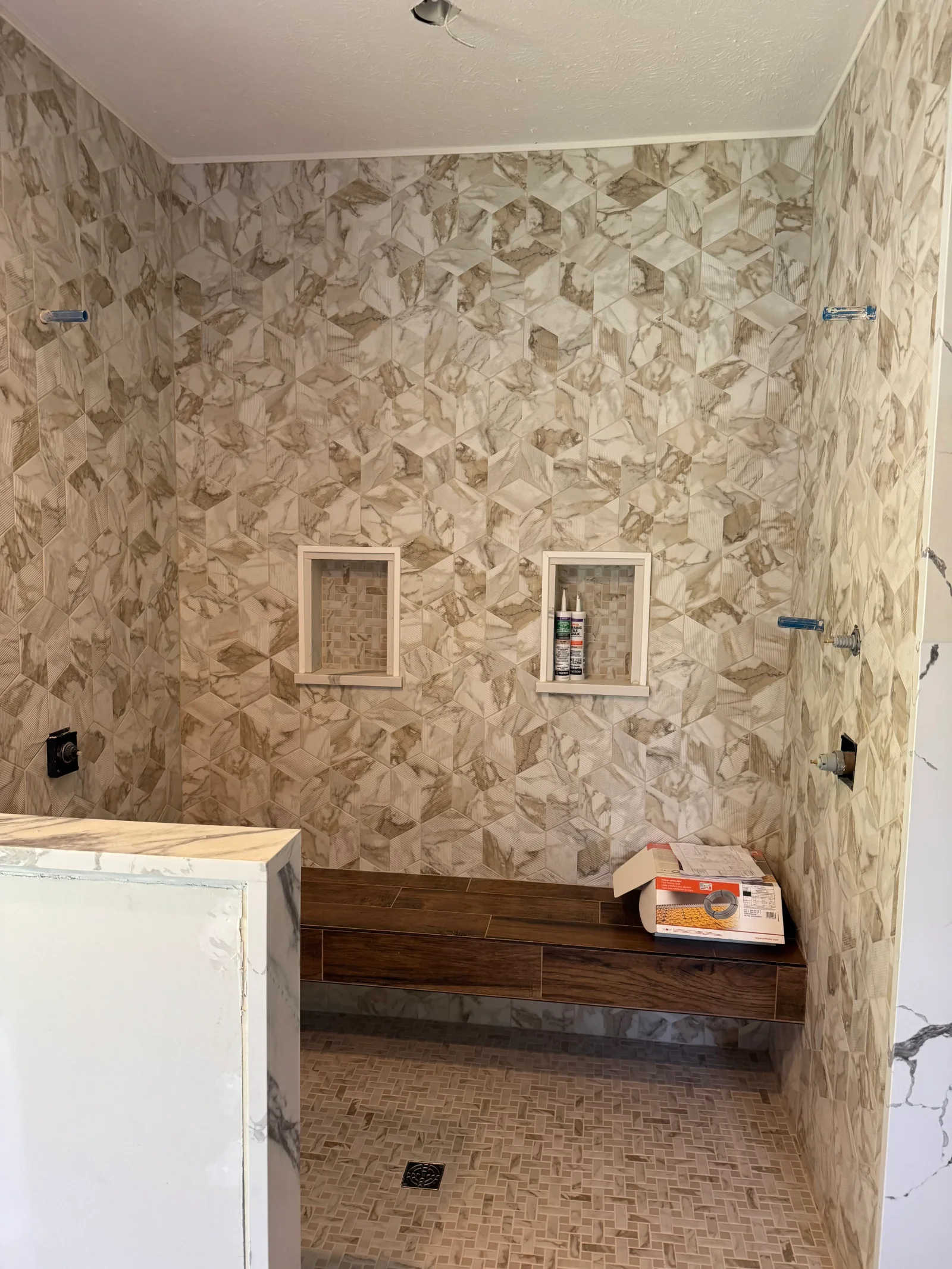 Marble tile shower with geometric pattern, wood bench, recessed niches, and herringbone floor