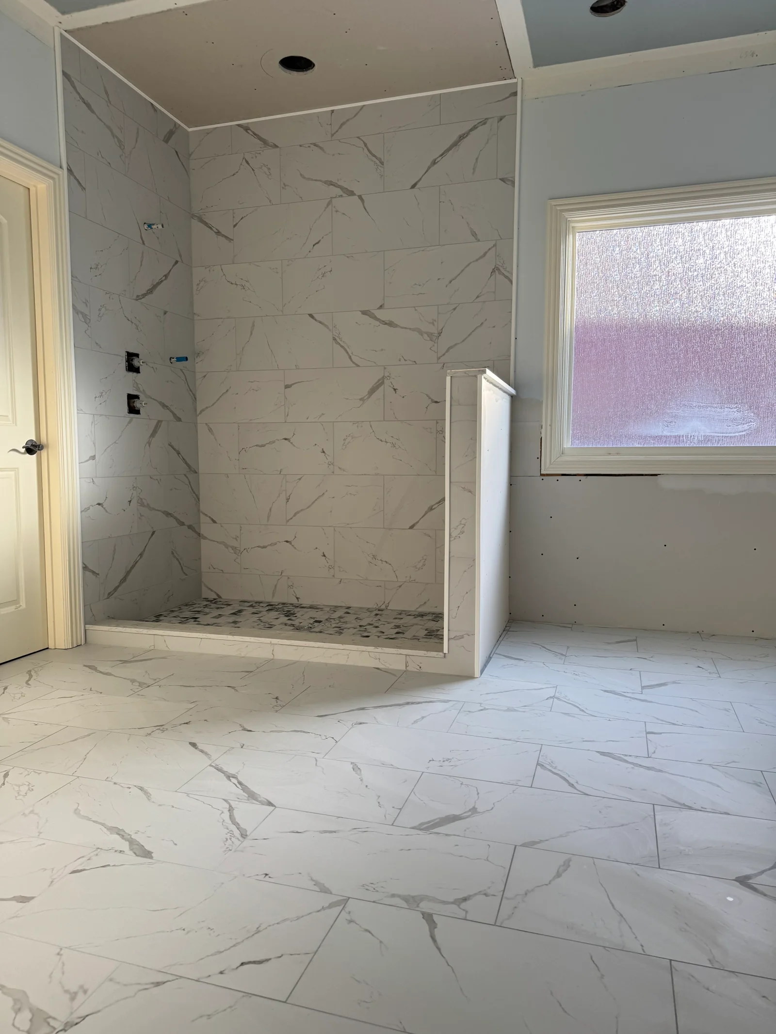 Marble-look tile bathroom with walk-in shower, herringbone floor, and frameless glass enclosure