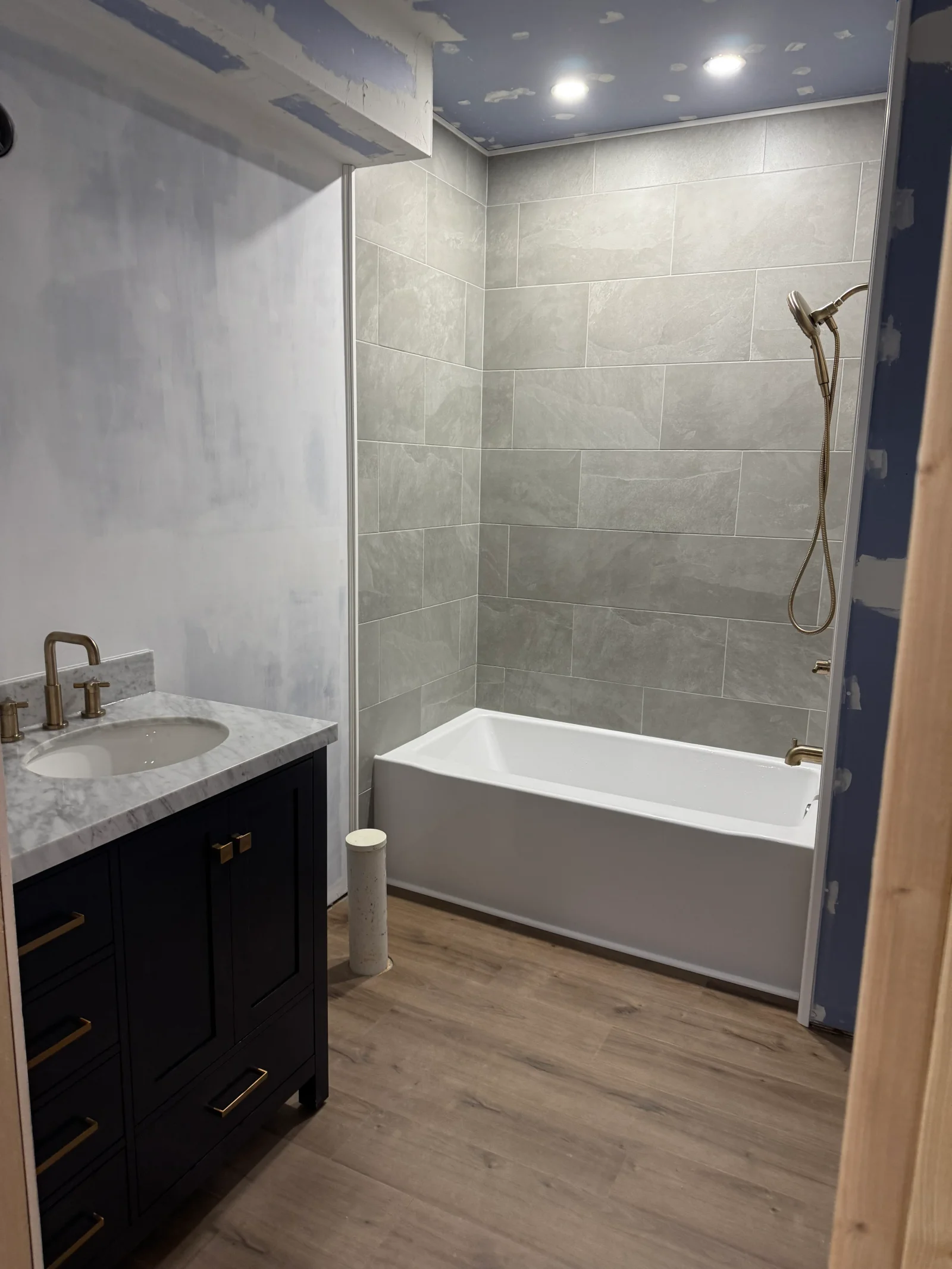 Bathroom with black vanity, marble countertop, gray tile tub surround, and glass enclosure