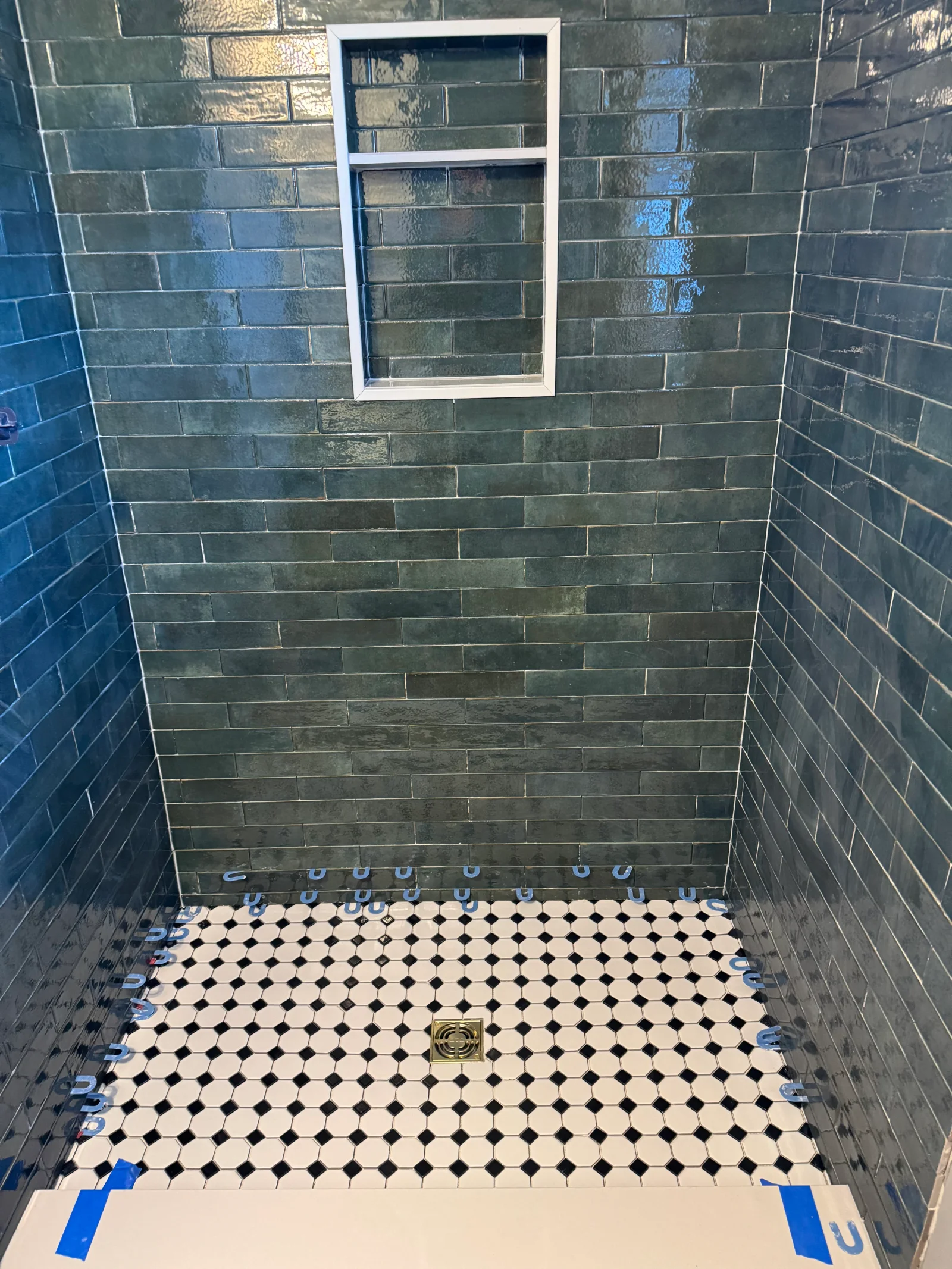 Dark green subway tile shower walls with white niche frame and black-white mosaic penny tile floor