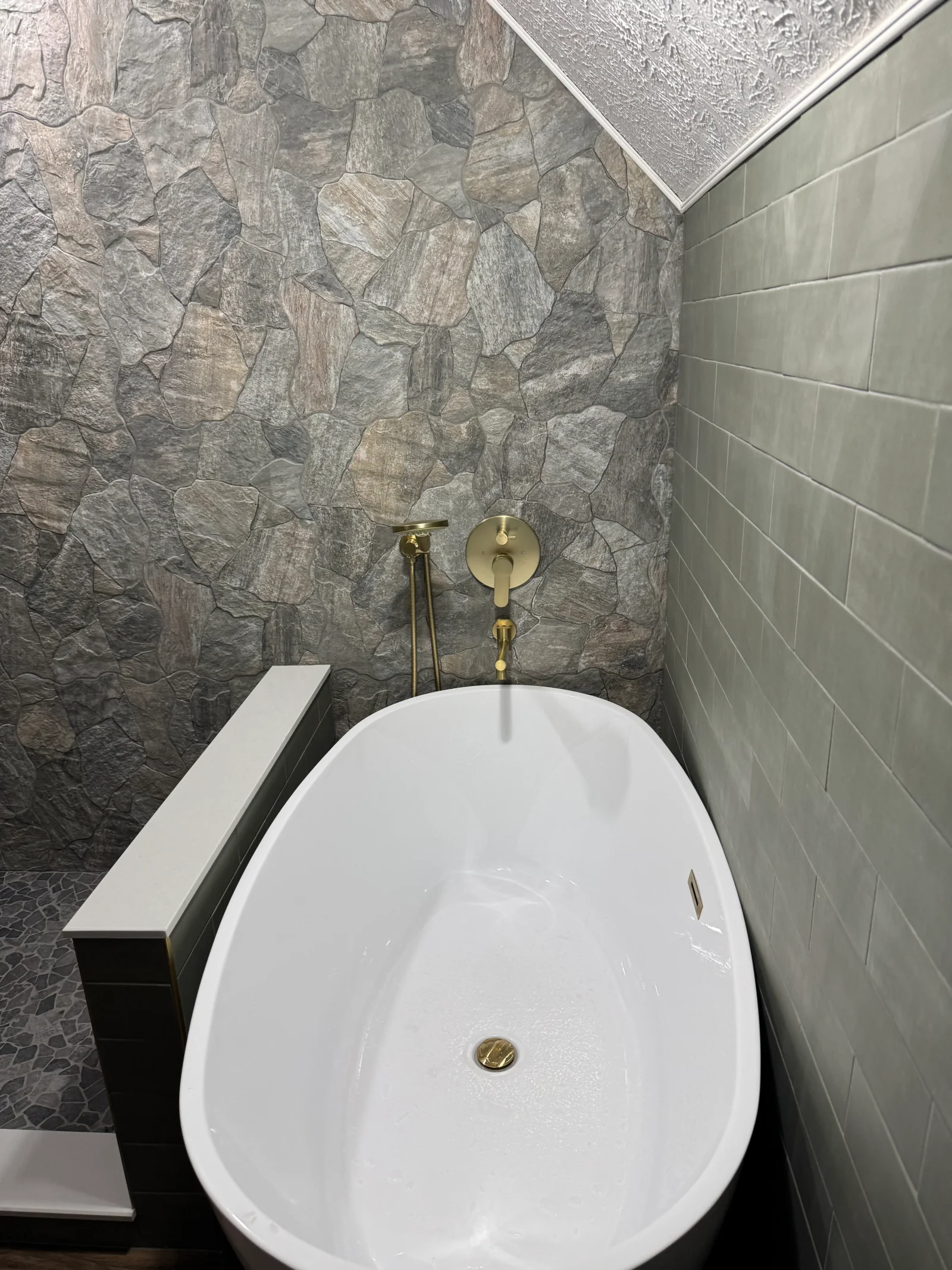 Freestanding white tub with slate stacked stone accent wall and brushed gold fixtures