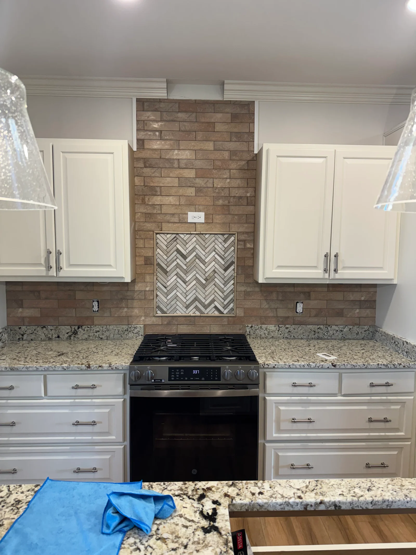 Brown brick tile backsplash with herringbone pattern accent around black gas range and hood