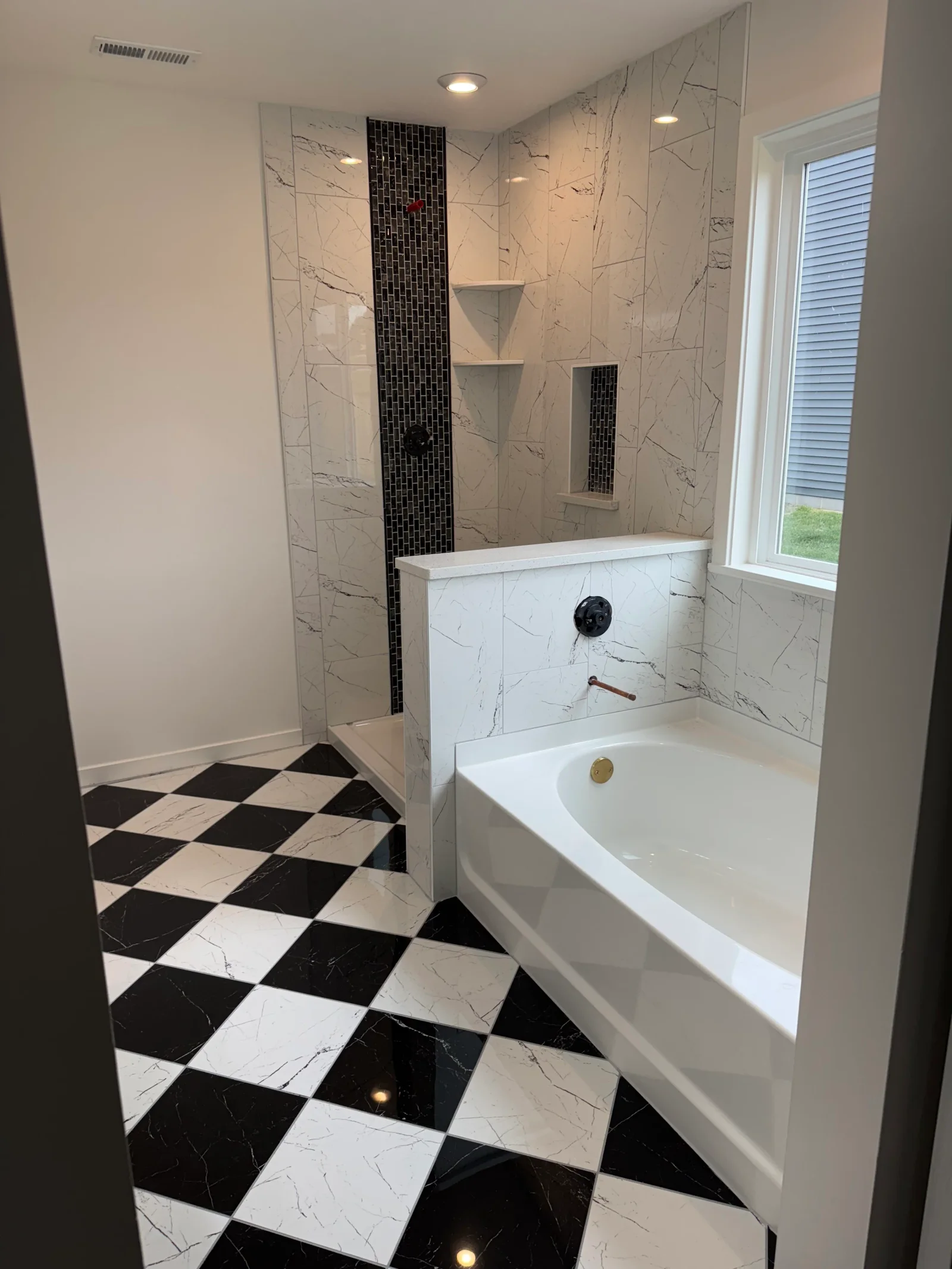 Marble tile walls with black mosaic accent, black and white diamond floor, soaking tub with tile surround and shelving