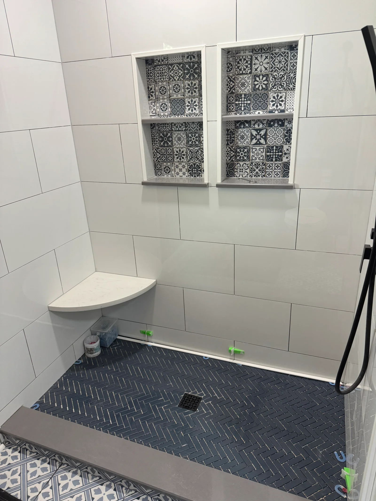 White subway tile bathroom with dual decorative niches, dark herringbone shower floor, and glass enclosure