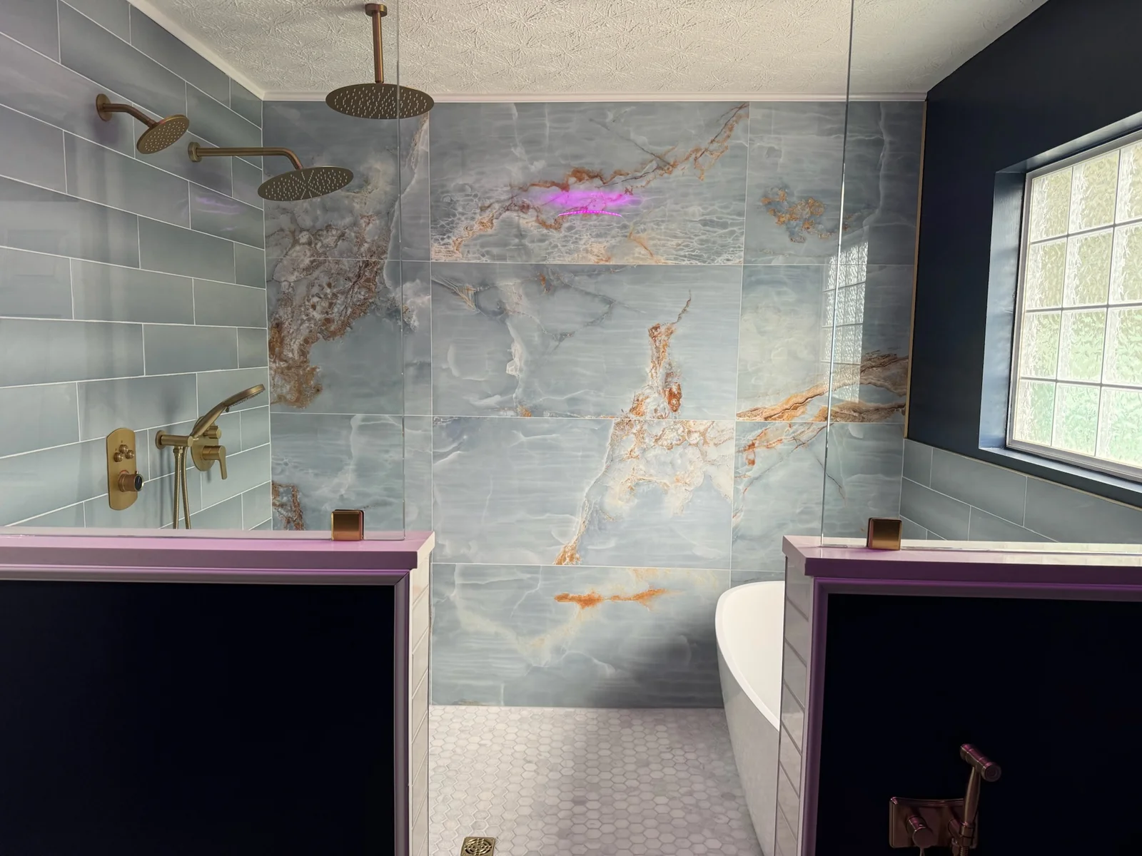 Custom tiled shower with marble accent wall, gold fixtures, and freestanding tub